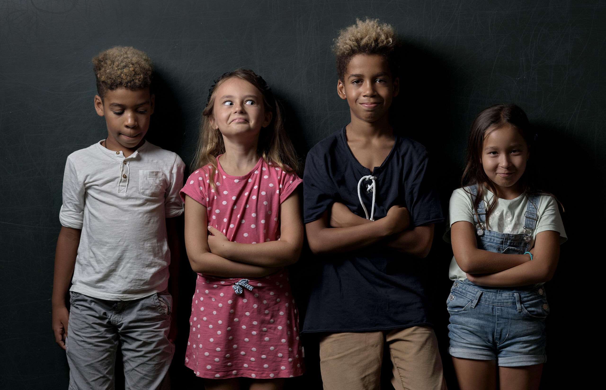 Four different-ethnicity kids standing on a dark wall background